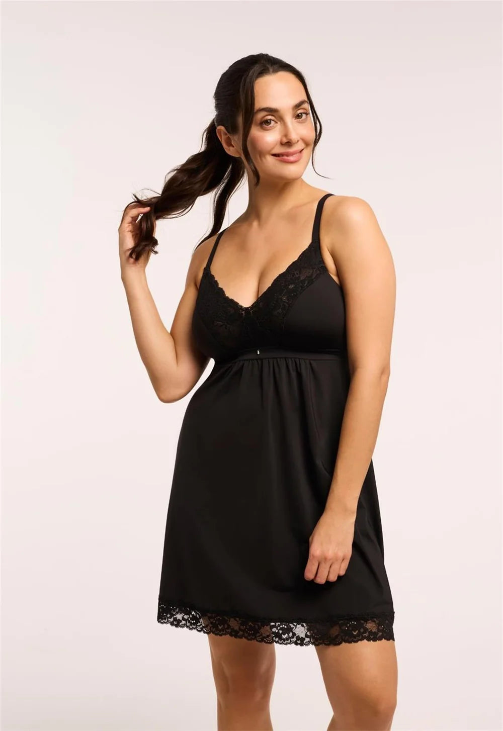 A woman modeling a black slip-style nightgown with lace trim on a light gray studio background.
