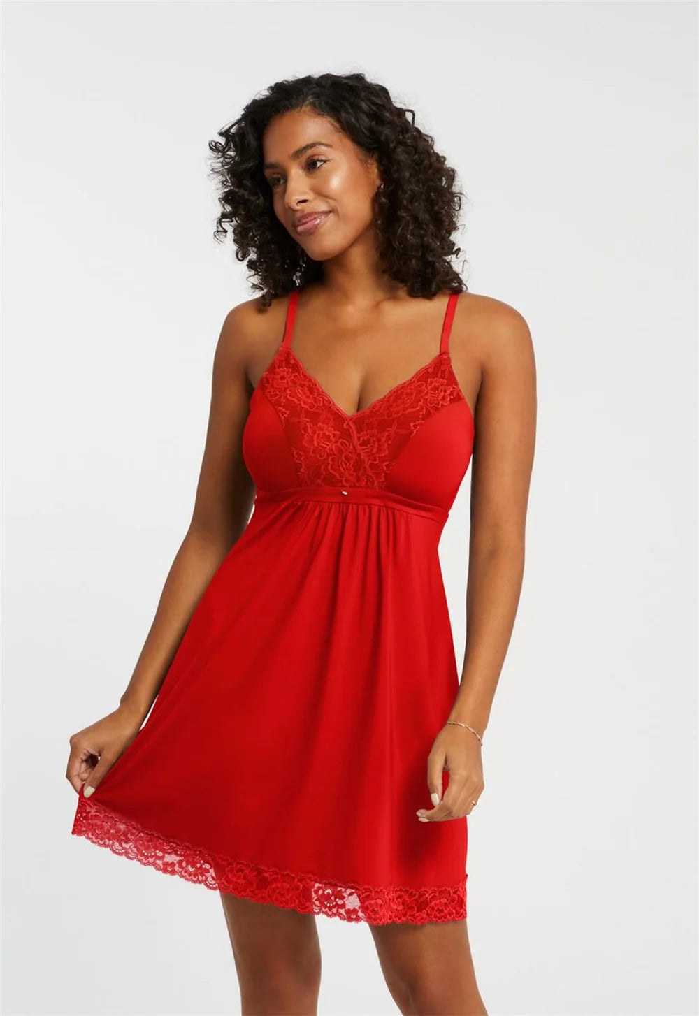 A woman modeling a red mini slip dress with lace trim and thin spaghetti straps against a plain light gray studio background.