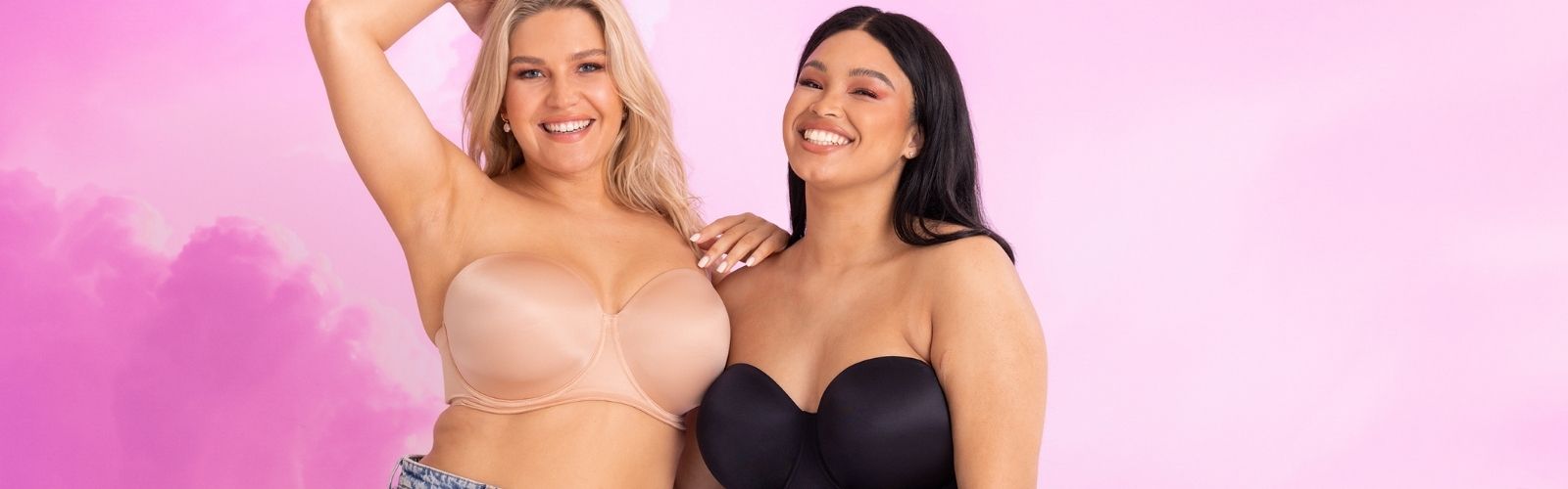 Model wearing Curvy Kate Smoothie Strapless Moulded Bra in Latte and Black (CK008109LAT & CK008109BLK), posing confidently in front of a soft pink cloud background – showcasing versatile, supportive style. Available in up to an UK K Cup. Bravo Bra Boutique
