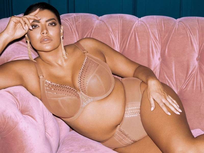Sophisticated Model on pink couch wearing Elomi EL8900CAT Plunge Bra and Brief in Cafe Au Lait.