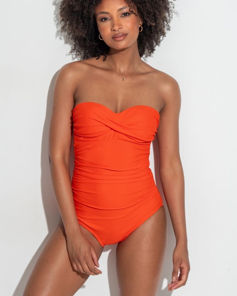 Model with brown curly hair wearing Pour Moi Santa Monica Orange Strapless one piece swimsuit.