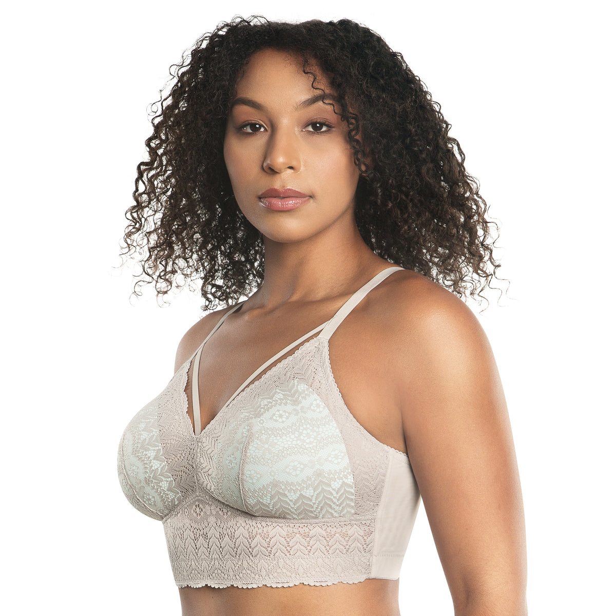 A woman with curly dark hair wearing a light beige lace bralette against a plain white background.